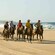 A group of horseback riders traverse alongside an unspoiled coastline